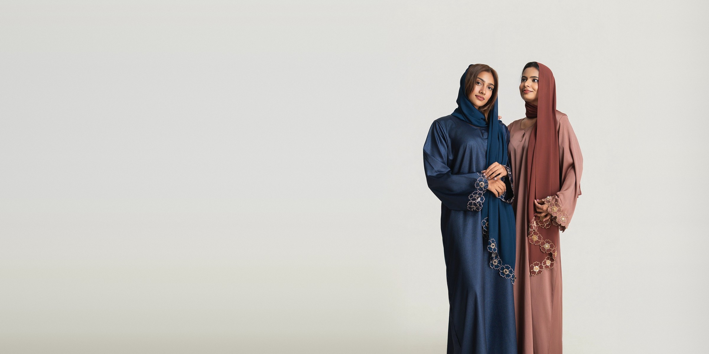 Two women in the Cedar and Amber abaya sets, navy and rosewood, with hand-embroidered floral sleeves